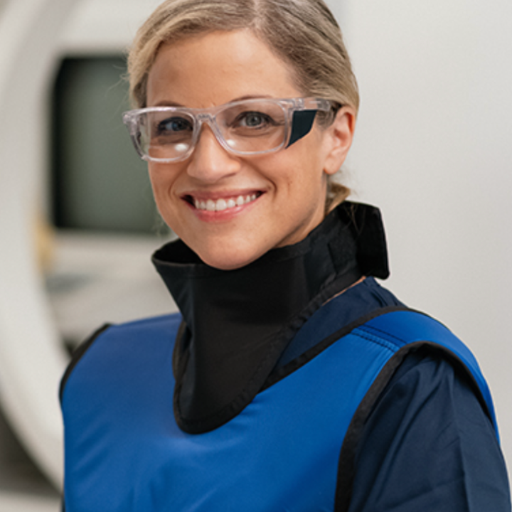 female wearing clear radiation protection glasses, black thyroid collar and a blue apron with a blurred background