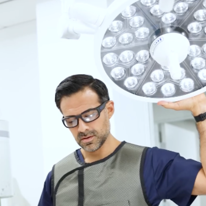 radiologist wearing lead glasses holding a large LED light fixture above his head
